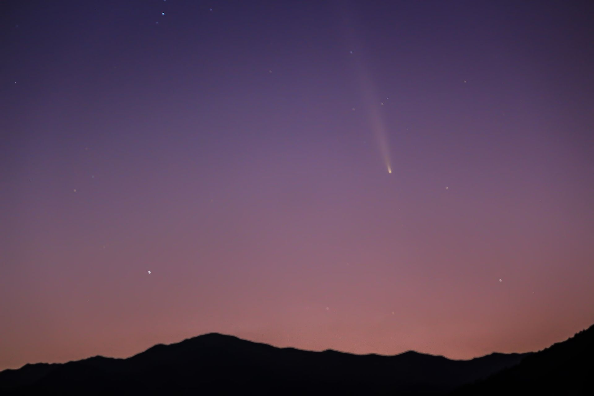 Comet C/2023 A3 (Tsuchinshan–ATLAS) visible in the night sky, captured with its glowing tail against a dark horizon.