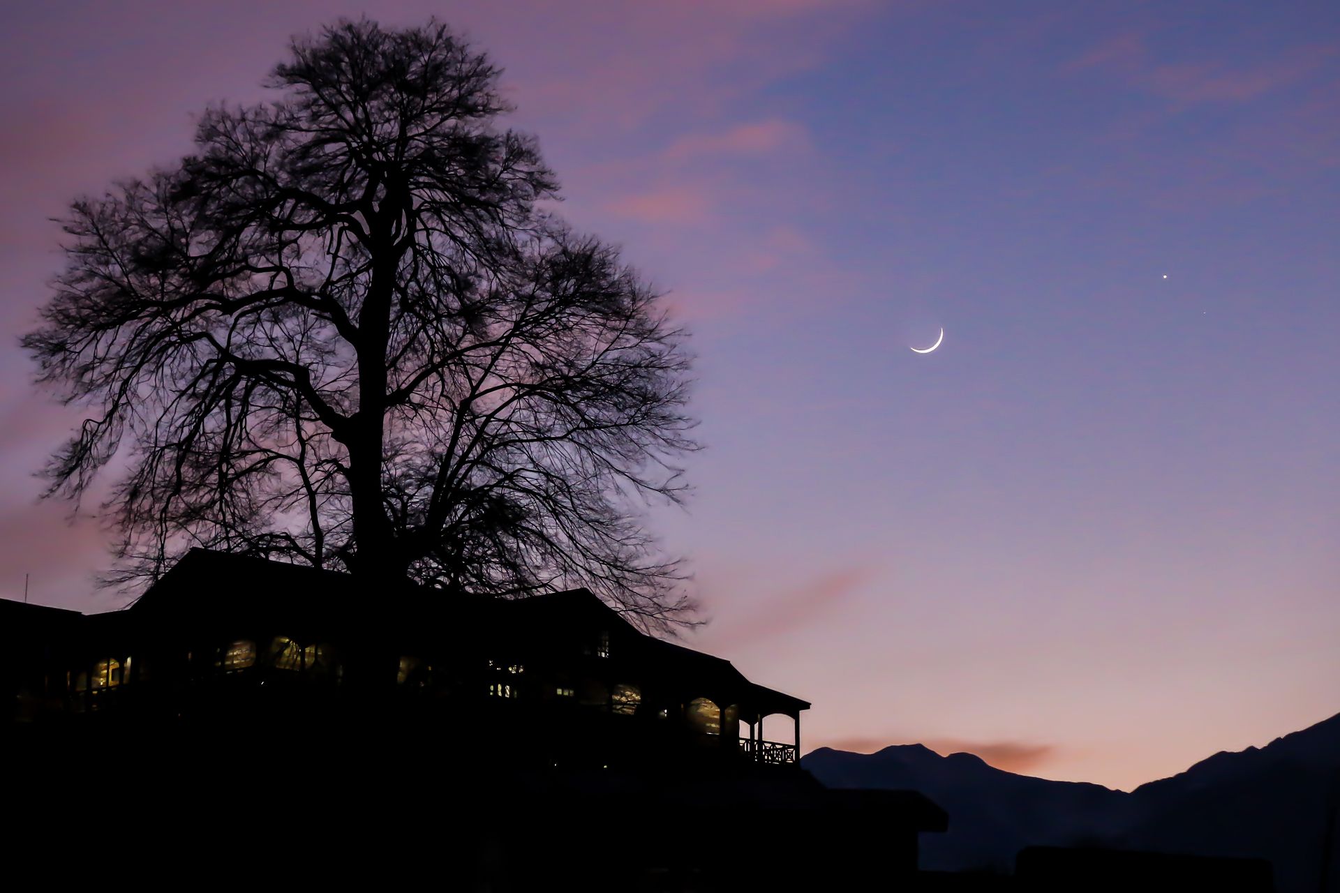 Naggar Castle in Himachal Pradesh with a crescent moon visible in the evening sky.